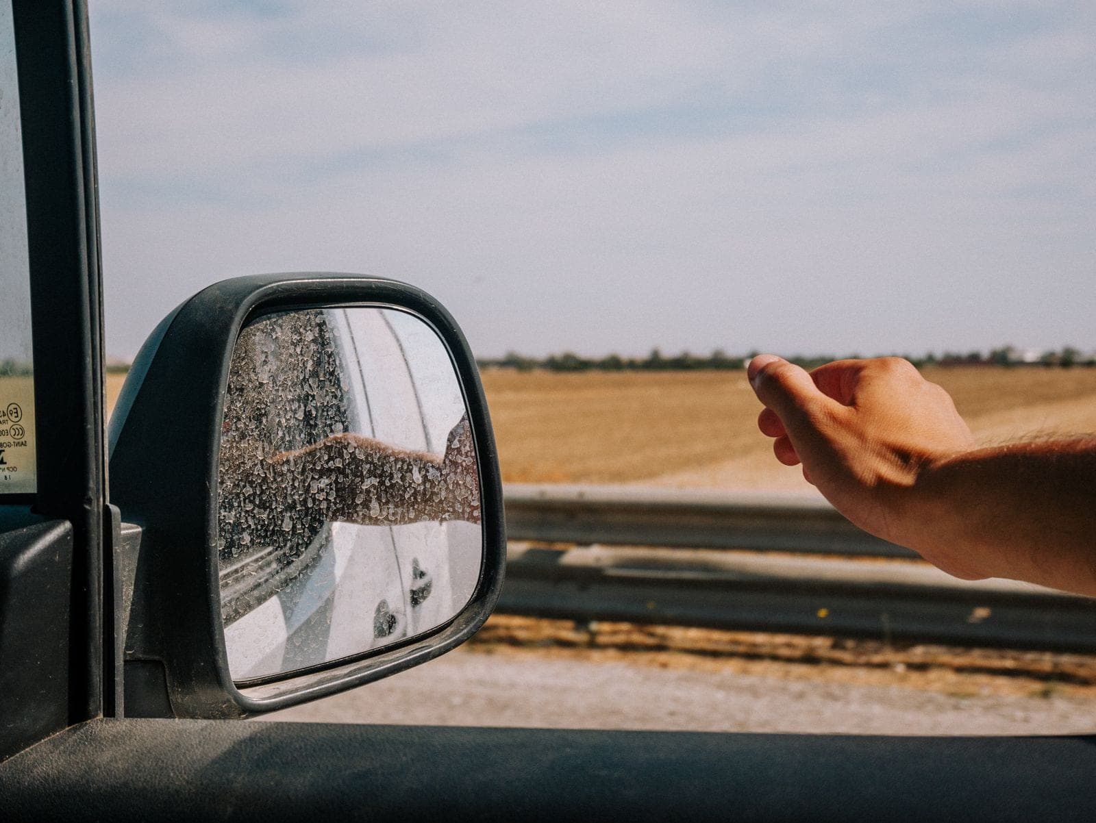 Open car door window and side mirror beside a field